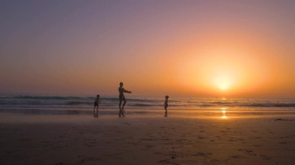 Silhouette of father with two children in the beach at sunset