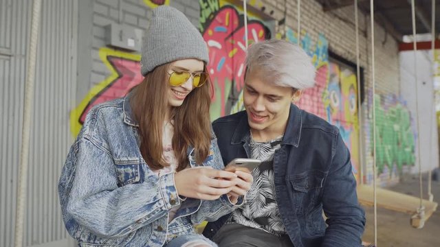 Young hipster couple smiling and having fun with a smart phone in urban background