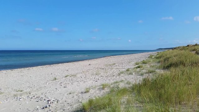 Liseleje Beach by the Tisvilde forest and coastal area on the Danish island of Zealand. A pristine spring morning with a sunny clear blue sky. Sand dunes with reeds and scattered beach stones.