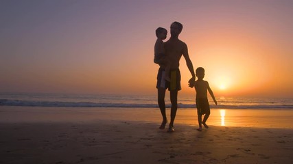 Silhouette of father with two children in the beach at sunset