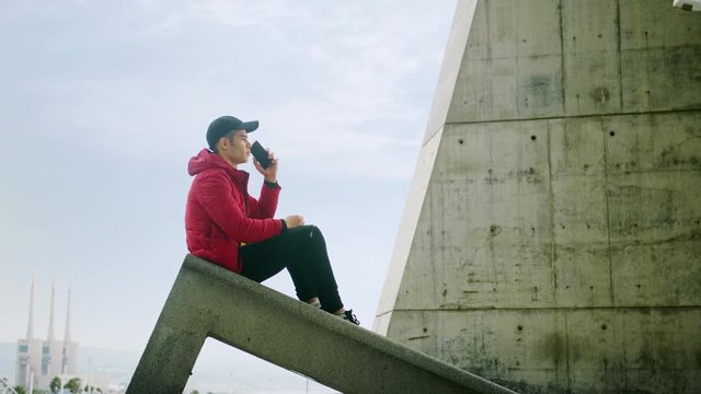 Young Attractive Trendy young Man interacting callling and messaging with a cell phone on an urban city background