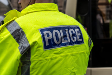 Rücken von Polizist mit neongelber Jacke mit der Aufschrift Police steht im Regen