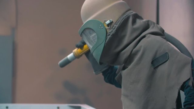 worker wearing mask using sand blast on metal surface in workshop