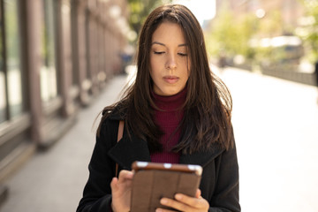 Young woman in city walking using tablet computer