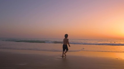 Silhouette of child running and playing  in the beach at sunset - freedom