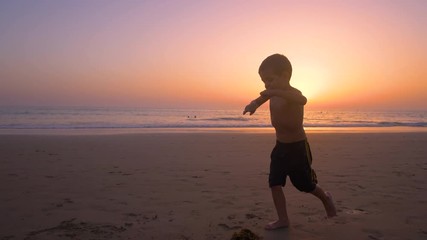 Silhouette of child running and playing  in the beach at sunset - freedom