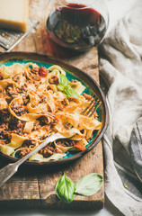 Italian traditional pasta dinner. Tagliatelle bolognese with minced meat, tomato sauce and parmesan cheese and glass of red wine over rustic wooden board background, selective focus