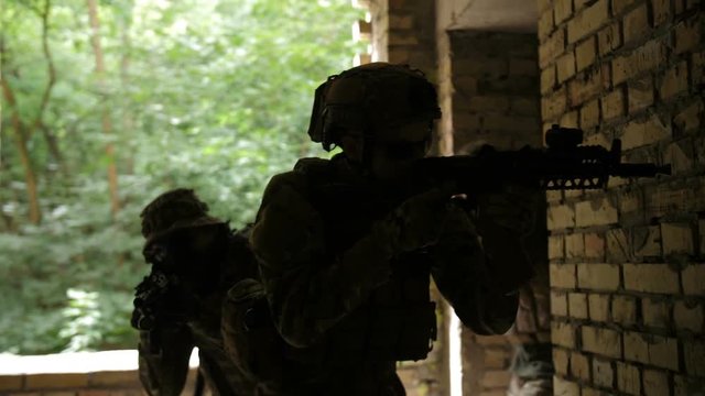 Closeup of elite squad of military soldiers in action during anti terrorism operation sneaking up to enemy building. Group of marines in camouflage holding guns and walking inside of ruined building.