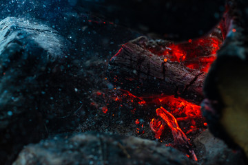 Smoldered logs burned in vivid fire. Atmospheric background with orange flame of campfire. Unimaginable detailed image of bonfire from inside with copy space. Whirlwind of smoke and ash close up.