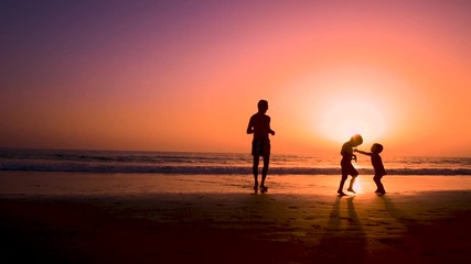 Silhouette of father with two children in the beach at sunset