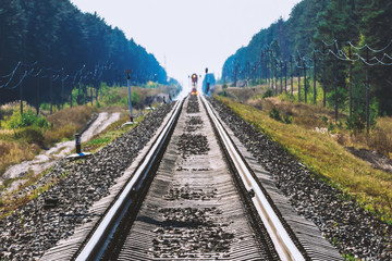 Fototapeta premium Mystic train travels by rail along forest. Railway traffic light and locomotive on railroad in distance. Mirage on railway track. Atmospheric landscape.