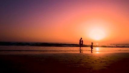 Silhouette of father with two children in the beach at sunset
