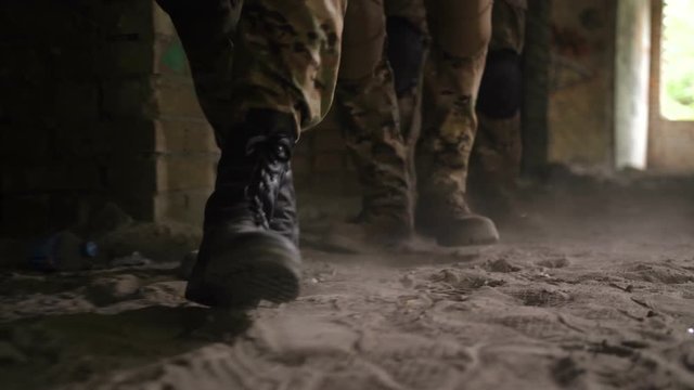 Close-up of soldier legs in old army paratroopers combat boots walking in dusty ruined building during military anti terrorism training. Special force rangers in action storming enemy building.