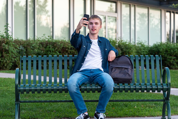 Male teenager taking a selfie with his phone while sitting on a bench.