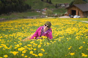 Naklejka na ściany i meble Active healthy woman having rest on beautiful meadow covered with flowers. Portrait of happy smiling young woman resting of mountains clearing during hike holidays