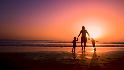 Silhouette of father with two children in the beach at sunset
