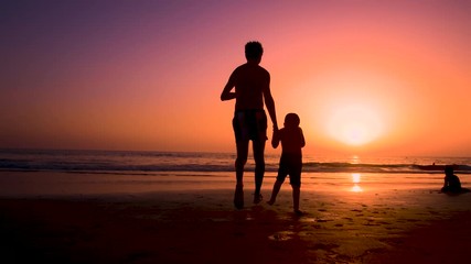Silhouette of father with two children in the beach at sunset