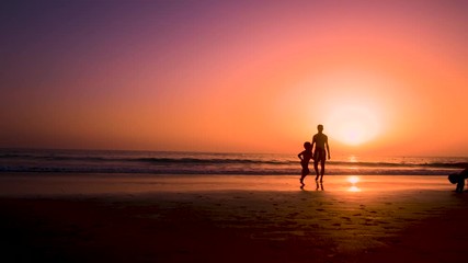 Silhouette of father with two children in the beach at sunset