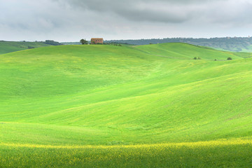 Fototapeta na wymiar Idyllic scenery of a farmhouse in green grassy fields with rolling hills on a cloudy spring day in Tuscany, Italy