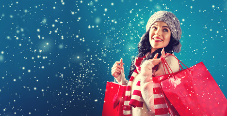 Happy young woman holding shopping bags in a snowy night © Tierney