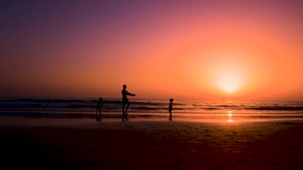 Silhouette of father with two children in the beach at sunset