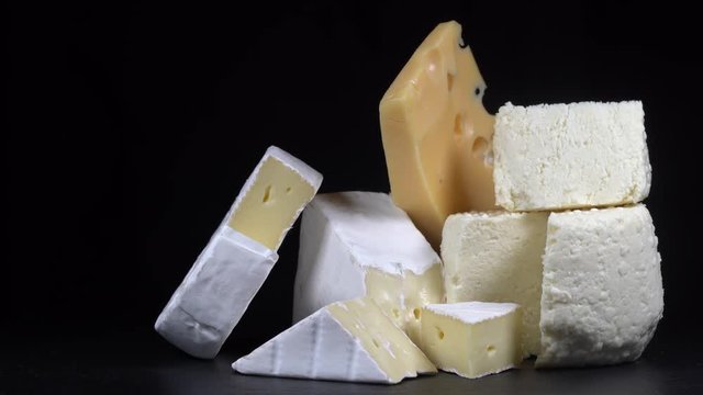 Assorted cheeses on black slate plate. Delicious pieces of different cheeses on black background, close up, macro. Rotating video