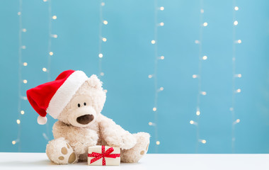 Teddy bear wearing a Santa hat and a gift box on a shiny light blue background
