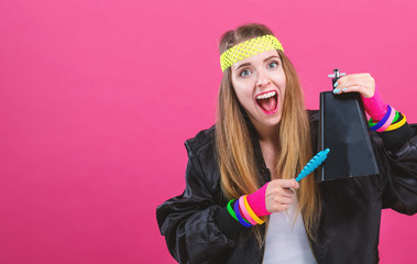 Woman in 1980's fashion playing a cowbell on a pink background