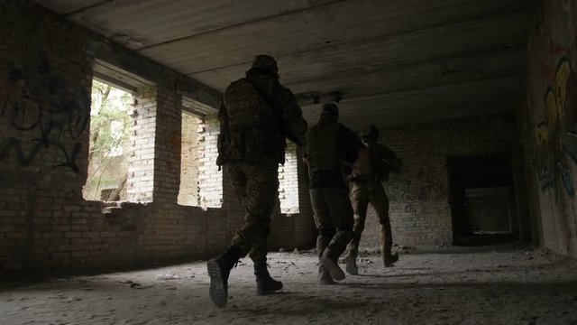 Army soldiers in full tactical gear with weapons intruding inside the building captured by enemy during military operation. Special forces rangers running to free hostage in abandoned building.
