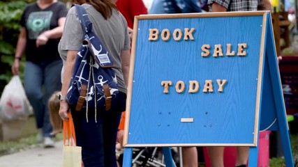 Local library has a book sale sign on a busy sidewalk.