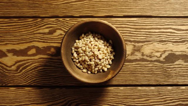 TOP VIEW: Peeled pine nuts appear in wooden cup and full this cup - Stop motion