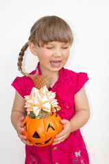 Little beautiful girl holding pumpkin with sweets in hands, on Halloween.