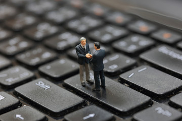 Selective focus of miniature business man handshake on the button Enter button keyboard of laptop as commitment and partnership concept.