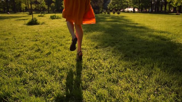 Woman feet running by grass in park. No face. Sunset or surise. Slow motion. Middle skirt, slender legs, barefoot.