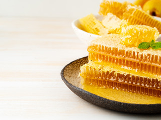honey in honeycomb, close-up, on brown ceramic plate, on wooden white rustic table, side view, copy space