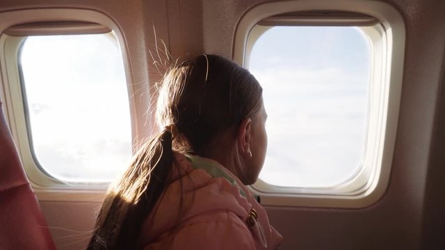 A young girl looks out the window of the aircraft. The girl enjoys the view from the window of the plane. 4k