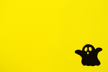 Holiday decorations for Halloween. Black paper ghost on a yellow background, top view.
