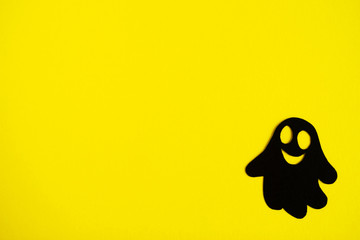 Holiday decorations for Halloween. Black paper ghost on a yellow background, top view.