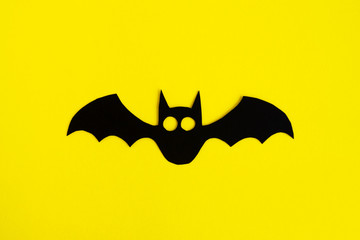 Holiday decorations for Halloween. Black paper bat on a yellow background, top view.