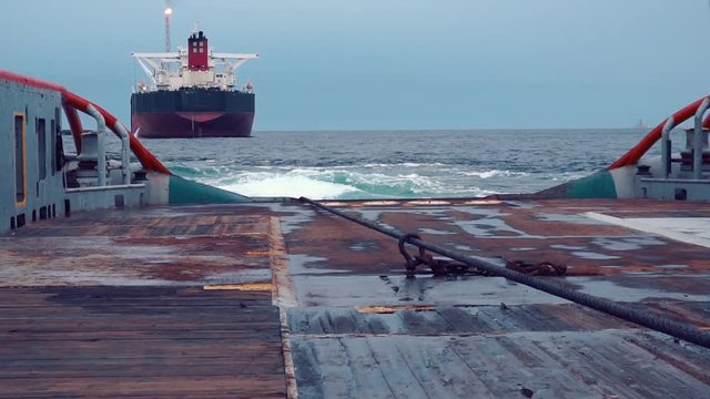 Anchor-handling Tug Supply AHTS vessel during dynamic positioning DP operations near FPSO tanker. Vessel is doing static tow tanker lifting. Ocean tug job.