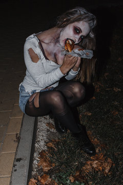 Woman eating burger with ketchup in the image of a zombie
