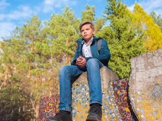 Teenager sitting on top of a rock. Autumn forest and blue sky background