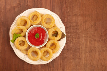 A photo of squid rings with a tomato sauce, shot from above on a dark rustic wooden background with a place for text