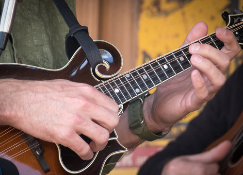 Closeup of a man's hands playing a brown wooden mandolin