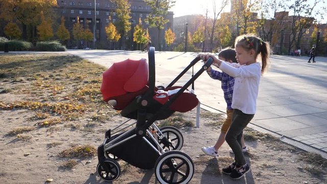 Brother and sister children pushing together the stroller with baby walking in a city