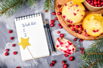 hand holds cranberry cupcakenotebook for records on the table. Cranberry cupcakes with a golden star topper lie on a wooden tray