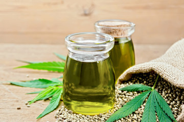 Oil hemp in two jars with sheet on wooden board