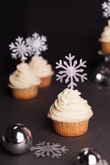 Fototapeta na wymiar sweets for christmas - Christmas cupcake with cream cheese decorated with shining silver snowflakes on black background