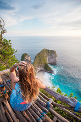 Woman sitting on the wood stand and looking to the green rocks shaped like dinosaur head