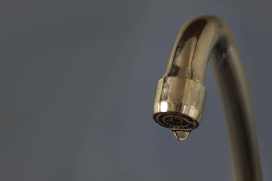 leaking water from the faucet on the grey background. Drop.Water saving.